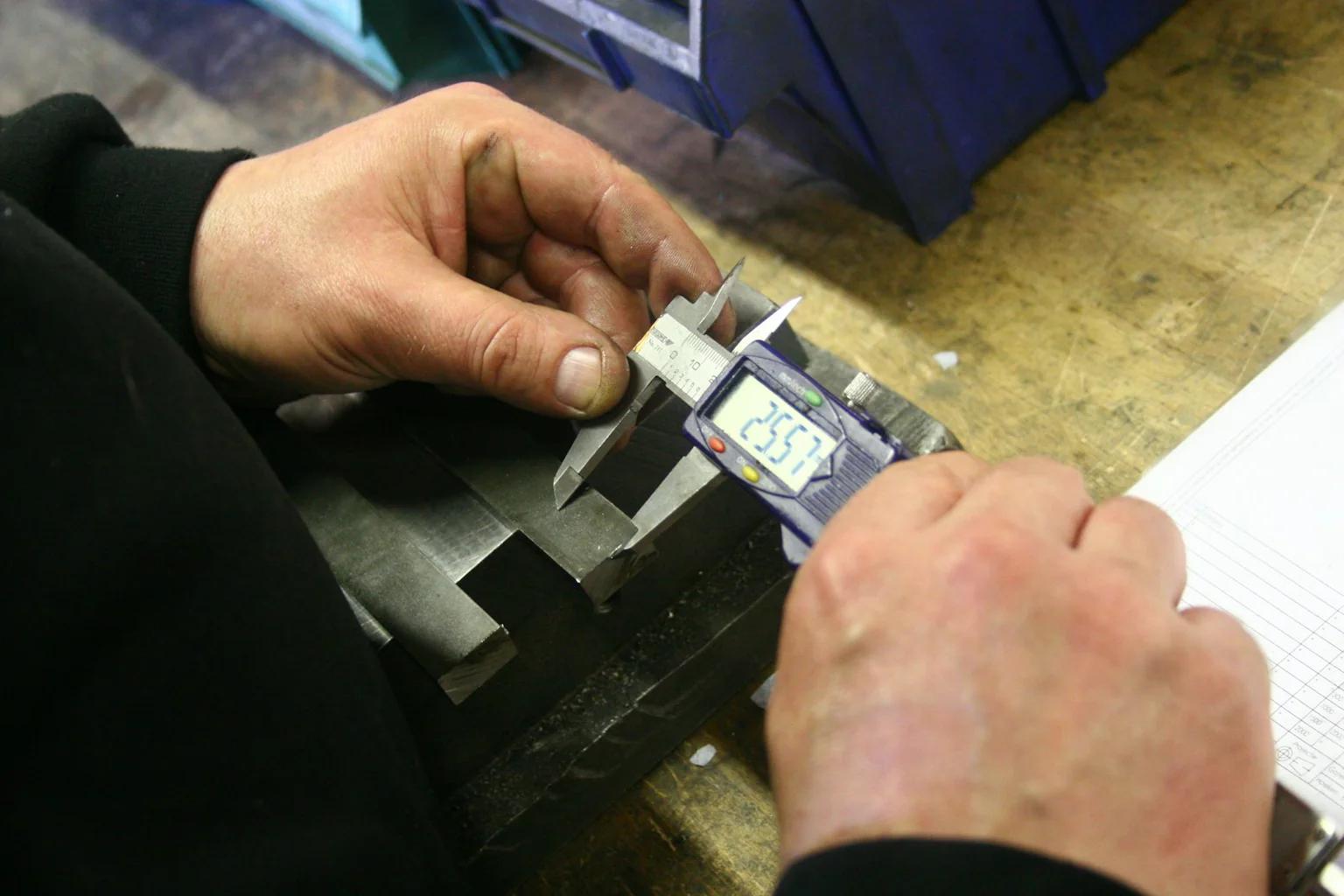 Operator checking a machined metal feature with digital calipers